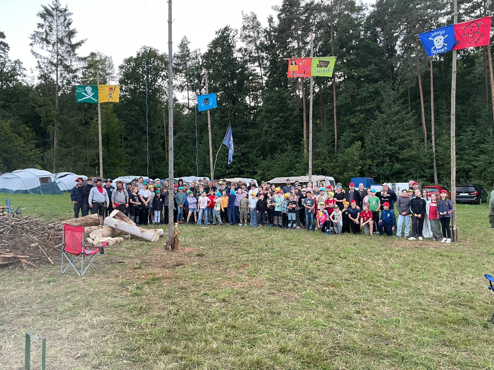 Großes Gruppenfoto des ganzen Zeltlagers zwischen Flaggenmasten und Wald