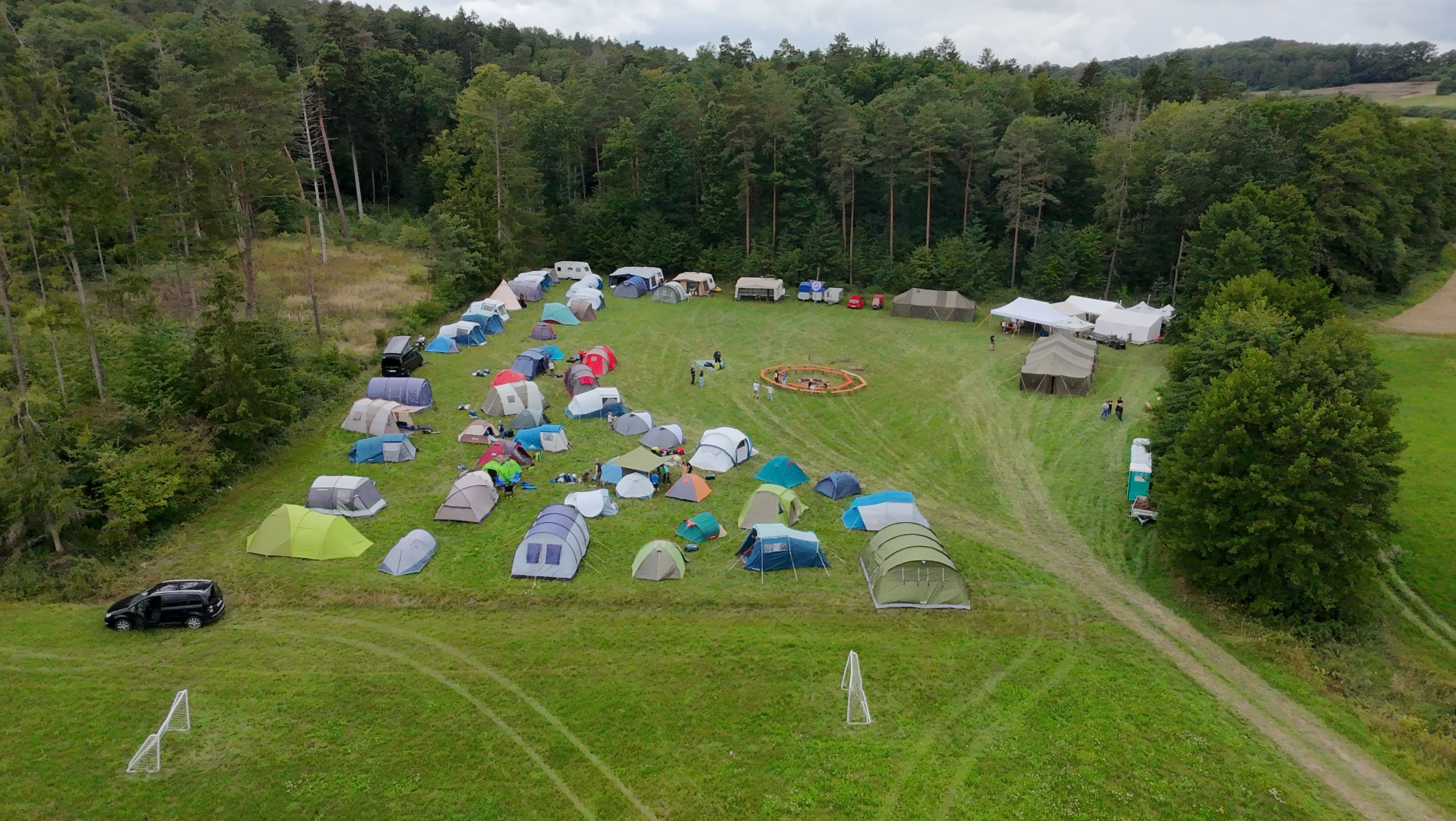 Drohnenaufnahme des gesamten Zeltplatzes auf der Wiese am Waldrand