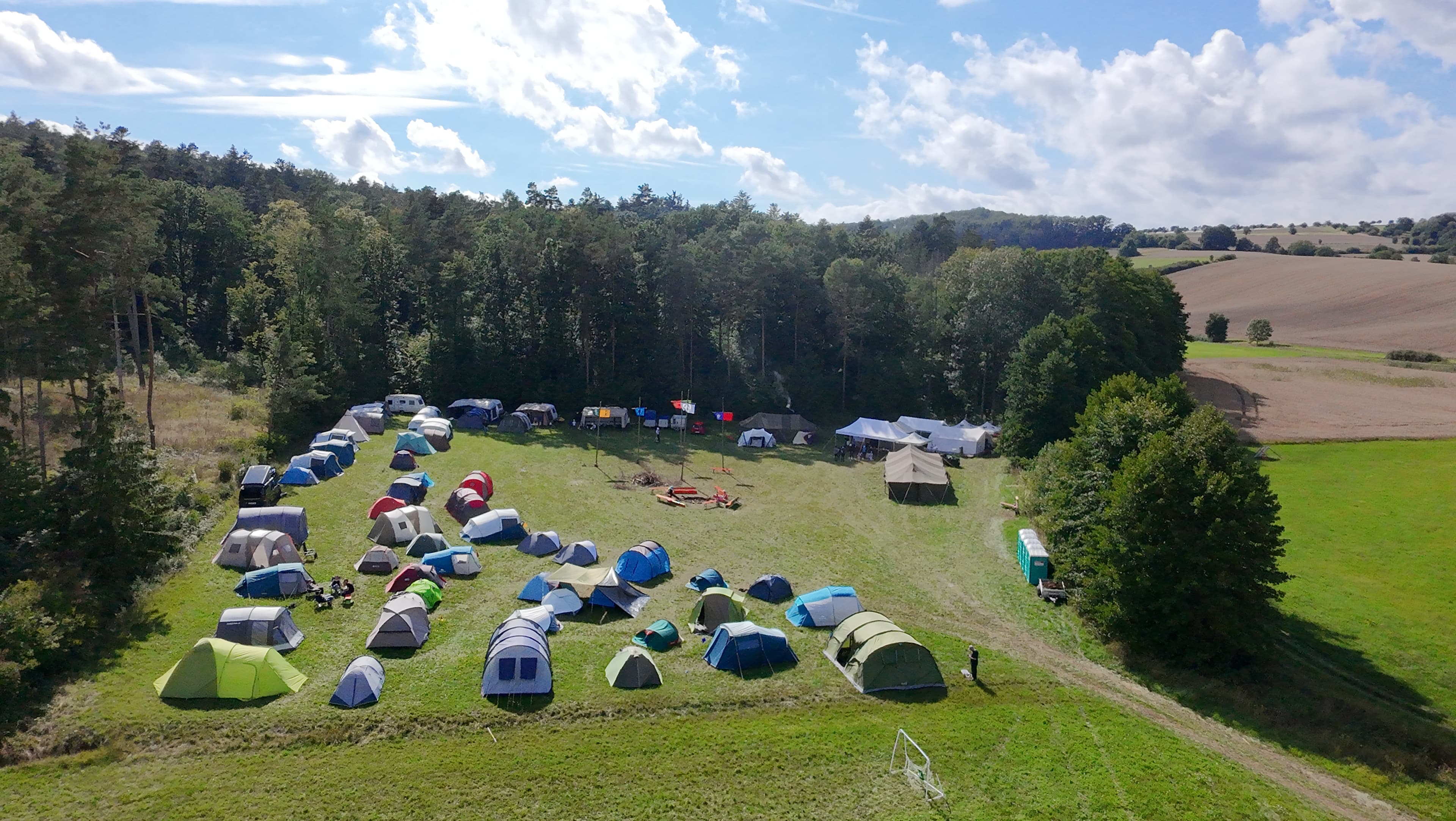 Luftaufnahme des Zeltlagers mit vielen bunten Zelten am Waldrand