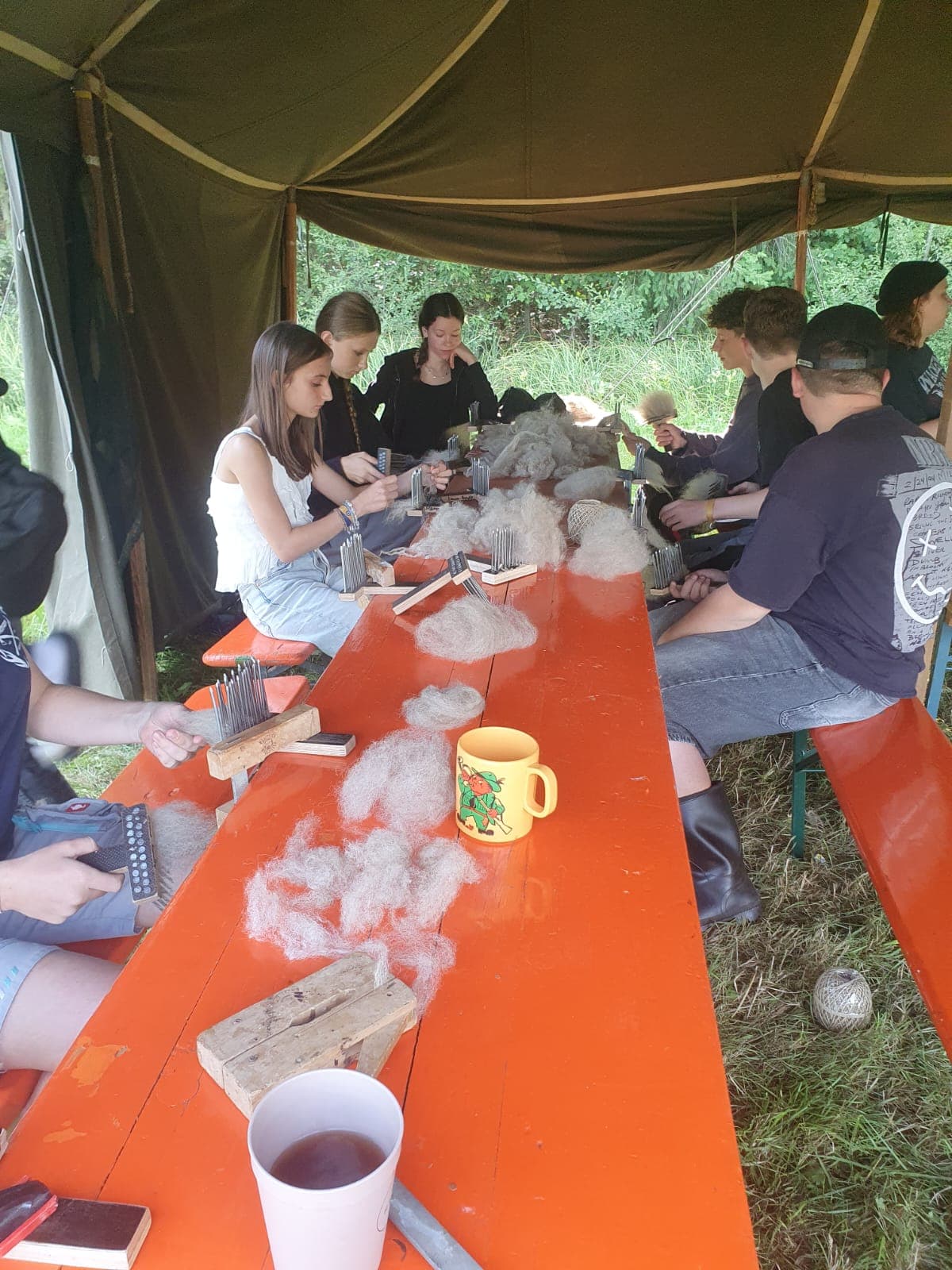 Jugendliche beim Woll-Workshop an langen Tischen im Gruppenzelt